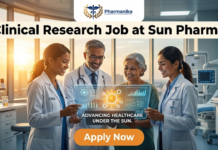 Latest Clinical Research Job at Sun Pharma | Pharmacy Graduates Don’t Miss This Opportunity!! A promotional job advertisement image for a Clinical Research Job at Sun Pharma, featuring the pharmanika logo at the top. The image depicts a diverse team of medical professionals—a man and two women in lab coats—standing in a modern, sunlit clinical facility. They are smiling and showing a futuristic holographic tablet to an older patient. The tablet displays medical data icons and the tagline "ADVANCING HEALTHCARE UNDER THE SUN." The main headline "Clinical Research Job at Sun Pharma" is prominently displayed at the top, and a large orange "Apply Now" button is located at the bottom. One researcher has "CRA" (Clinical Research Associate) embroidered on her lab coat.