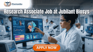 Research Associate Job at Jubilant Biosys | M Pharm Candidates Research Associate Job at Jubilant Biosys | M Pharm Candidates. A professional 1280x720 featured image for a "Research Associate Job at Jubilant Biosys." The scene features a female scientist in a white lab coat working in a bright, modern laboratory, pointing at a large monitor displaying colorful 3D molecular structures and research data. The Biotecnika logo is at the top center, and a prominent orange "Apply Now" button is at the bottom.