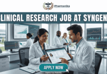 Latest Clinical Research Job at Syngene – M.Pharm & Pharm.D Candidate Apply Today! Latest Clinical Research Job at Syngene Apply Today! A featured image for a job page, part of Biotecnika, showcasing a clinical research position at Syngene. At the top center is the Biotecnika logo, with the text 'Your Bio Resource'. The main bold title is 'CLINICAL RESEARCH JOB AT SYNGENE'. The background features a detailed, realistic photograph of a diverse team of five scientists and professionals (two women, three men) collaborating in a modern, well-equipped laboratory, looking collaboratively into a computer monitor showing data charts, graphs, and a detailed 3D molecular structure. The lab has advanced scientific instruments, beakers, and shelves, visible next to a large window. The overall scene conveys scientific innovation, teamwork, and professionalism. At the bottom center, there is a prominent orange rectangular button labeled 'Apply now'.