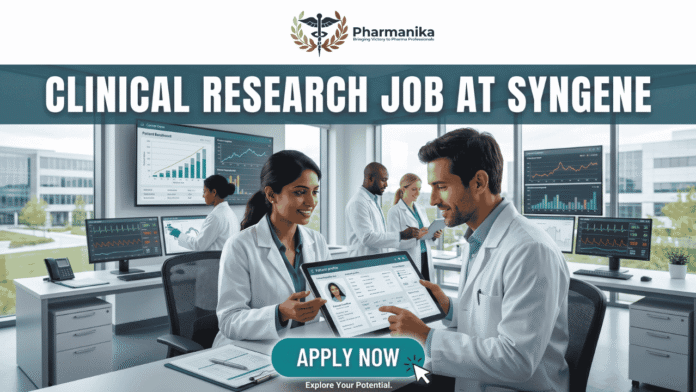 Latest Clinical Research Job at Syngene Apply Today! A featured image for a job page, part of Biotecnika, showcasing a clinical research position at Syngene. At the top center is the Biotecnika logo, with the text 'Your Bio Resource'. The main bold title is 'CLINICAL RESEARCH JOB AT SYNGENE'. The background features a detailed, realistic photograph of a diverse team of five scientists and professionals (two women, three men) collaborating in a modern, well-equipped laboratory, looking collaboratively into a computer monitor showing data charts, graphs, and a detailed 3D molecular structure. The lab has advanced scientific instruments, beakers, and shelves, visible next to a large window. The overall scene conveys scientific innovation, teamwork, and professionalism. At the bottom center, there is a prominent orange rectangular button labeled 'Apply now'.